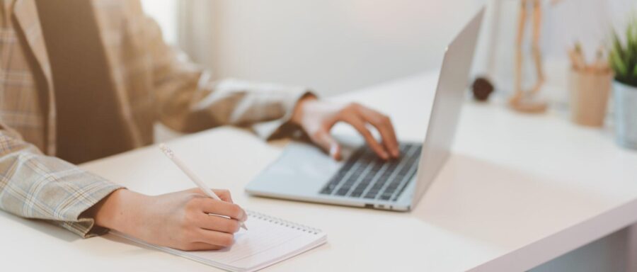 Businesswoman typing on laptop and writing on notebook