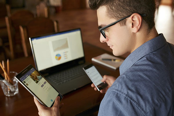 Attractive man in glasses working with multiple electronic internet devices min
