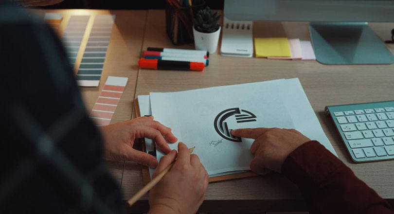 Creative team collaboration on logo design with sketch color palette and digital tools in modern office setting